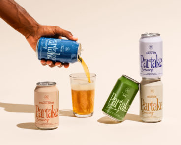 toronto-non-alcoholic-drinks-partake A hand pours a can of Partake non-alcoholic beer into a glass that is surrounded by other cans of Partake